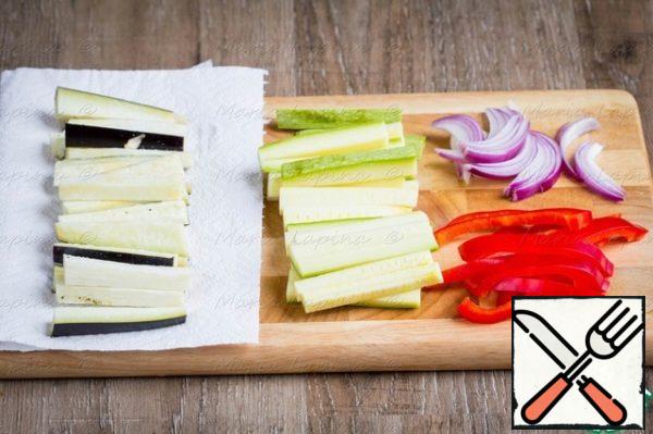 Prepare the vegetables for baking. Cut the eggplants into cubes, put them on a paper towel and add salt. Cut the zucchini into slices, onion and pepper into half rings or feathers.