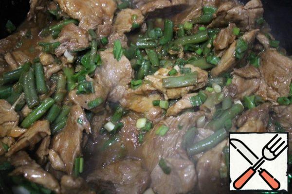 The meat has almost boiled off the liquid. It is allowed to have 2-3 tablespoons on the bottom. Add the beans and finely chopped green onions to the meat. Mix everything and simmer for 3 minutes. Then add the oyster sauce, mix everything quickly and simmer for another 30 seconds.