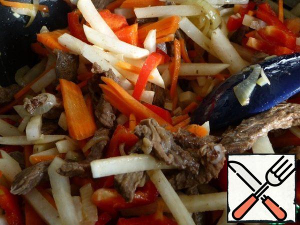 Add onions to the fried meat, continue to fry.
Then add carrots, radishes. Fry and stir.
Add the bell pepper and continue to fry.
Everything is fried over high heat, but it should not burn.