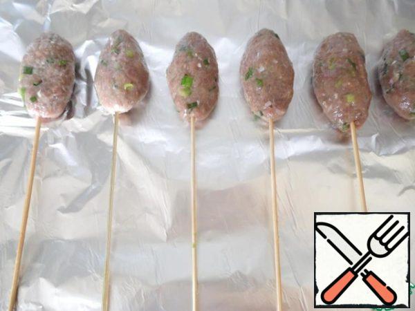 Then, divide the minced meat into three parts with a spatula, separate 1/3 of the minced meat and fry a little. Connect with 2/3 parts of raw minced meat, mix well, form a thick sausage of minced meat with a diameter of 3-4 cm and a length of 5-6 cm. Put them on wooden skewers.