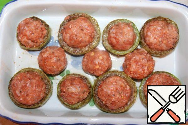 In a baking dish put the fried slices of zucchini, put the mixed minced meat in them. Roll the meatballs out of the minced meat and put in the form.