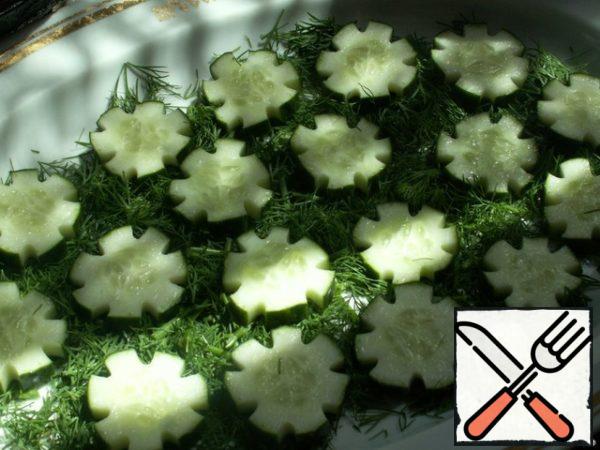 It is better to take an oval or round dish.
Sprinkle with finely chopped dill.
Cucumbers cut into rings with a thickness of 0.5 cm, put on the dill. 