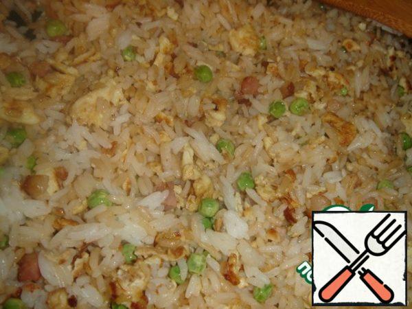 Add the boiled rice and stir in the pan. Fry everything together for a few minutes until the rice is warm. At the end, add the pre-fried bacon, pour soy sauce, season with salt and pepper.