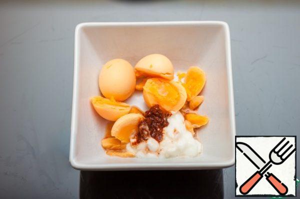 Cut the eggs in half, divide into whites and yolks, add yogurt and adjika to the yolks, mash with a fork.
