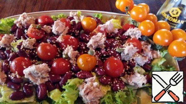 Put a layer of lettuce leaves on the dish, sprinkle with dressing. Place the beans with tomatoes and tuna slices on top, pour with dressing, sprinkle with capers and slightly roasted sesame seeds.