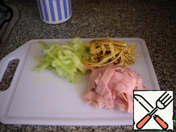 Whisk small eggs into a soft mousse, add salt and cook two thin omelets in a frying pan with butter. Do not spare the butter, the pancake will turn out softer.
While the eggs are cooling, cut the cucumber with a vegetable peeler or a knife into long strips, and also cut the ham. Add salt to the cucumber, but do not pour the juice. The cooled pancakes are also cut into strips.