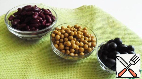 Drain the liquid from the beans, peas and olives through a colander. Cut the olives into halves.

