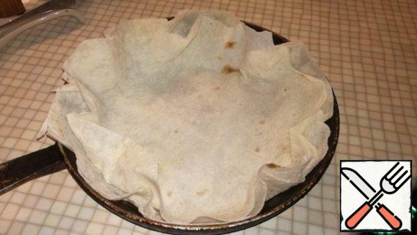 Take a round dish for baking, I have a frying pan size 26×26. Grease lightly with vegetable oil. Lay two sheets of pita bread. And once again lightly coat with vegetable oil pita bread. If lavash is large or not round, cut the edges with scissors.