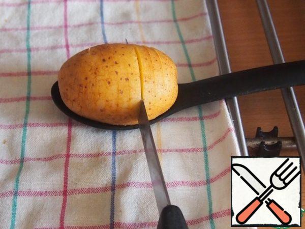 Cut potatoes into thin slices without cutting through. To do this, I use a deep spoon. Put a potato in a spoon and cut slices with a sharp knife, so the potatoes do not cut through.