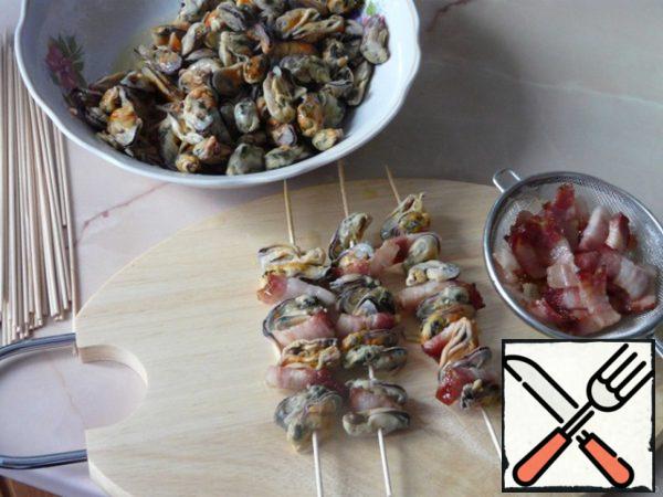 Thaw mussels, rinse with cold water,drizzle with vinegar and oil, let it stand marinated. To fry small pieces of bacon. String mussels and bacon do on skewers. If you are going to cook on an open fire-on metal skewers.