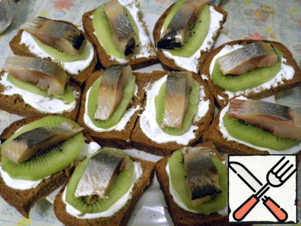 Peel the herring from the skin and bones, cut into long thin slices and put it on top of the kiwi. The canapes are ready, decorate with herbs before serving.