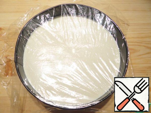 Pour the curd mass into the form with the base, cover the top of the form with a film.