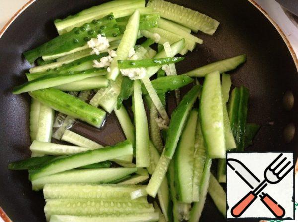 In a hot frying pan pour the oil and put the cucumbers, cut into thin slices. Garlic skip through the press, salt lightly.