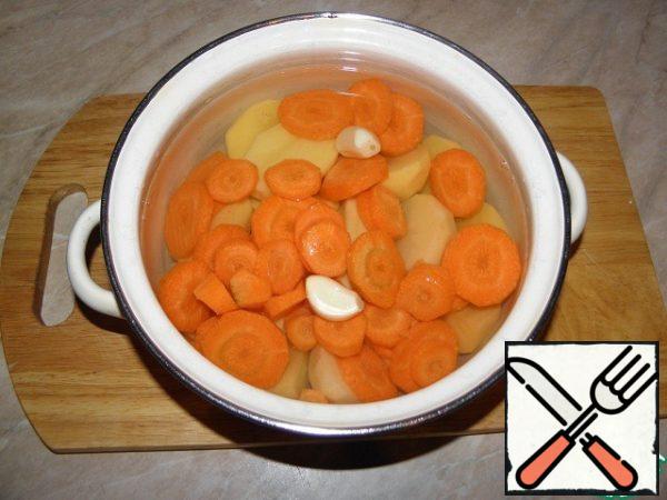 Peel potatoes, chop, cut carrots into 1-1. 5 cm cubes, peel garlic from cloves, put in a saucepan, add water (not too much water), bring to a boil, add salt, boil well until cooked.
