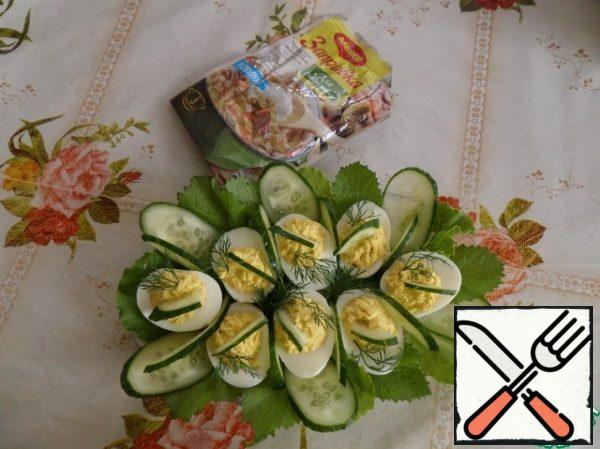 On a plate spread the lettuce. On salad leaves lay out the egg whites (halves). In half of egg we spread the yolk mass. Decorate with herbs and sliced cucumber.
