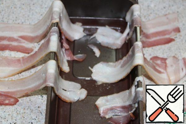 In a narrow rectangular heat-resistant form, lay out the bacon so that the strips hang over the edge on both sides.