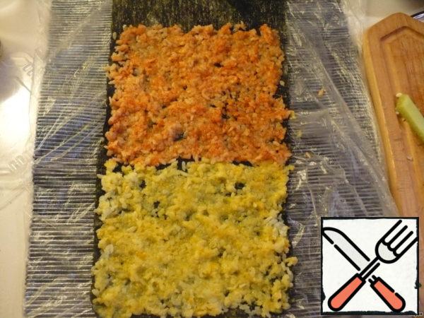 And now - the most beautiful - mosaic. Divide the rice into 2 equal parts. Those who have flying fish caviar and black sesame can mix each of these parts with these components. I rolled one part in turmeric, the other in paprika. We take two sheets of nori, put them on top of each other along the length, glue the edges with water. We put yellow rice on the first sheet, then red. I couldn't find my bamboo mat, my daughter was "playing" somewhere, so I had to put a thick napkin in the bag.
