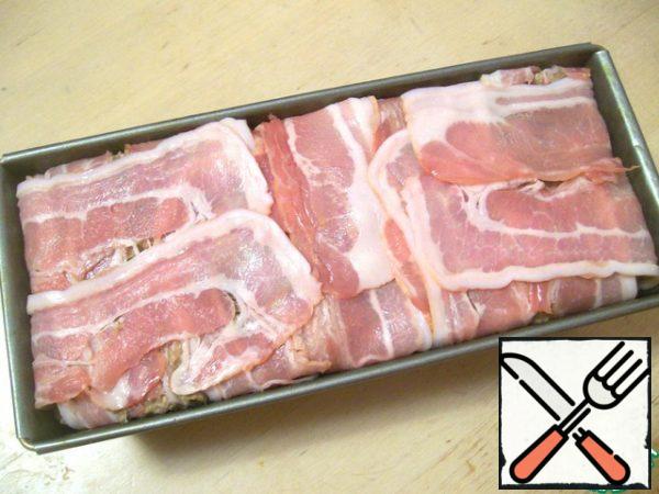 Now take the form in which we bake terrine. I have rectangular. A little grease it with vegetable oil, line the bottom and sides with strips of bacon so that they hung out and we could then close them on top of our terrine. Spread tightly minced in the form, close the top strips of bacon. It should look something like this.