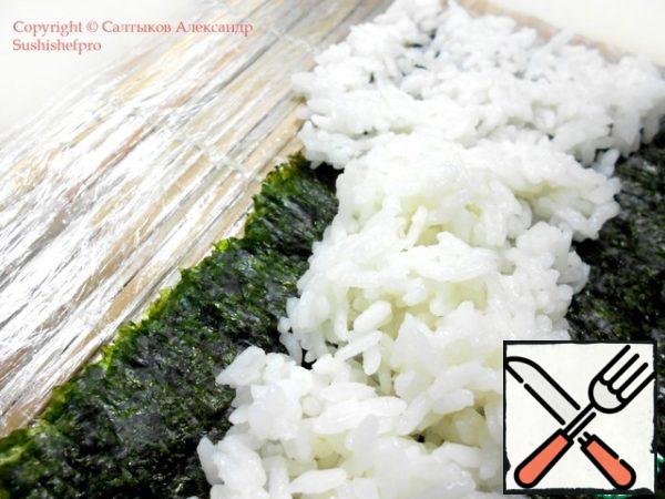 Carefully distribute the rice so that it protrudes a little from one edge, about 1 cm: look at the photo.