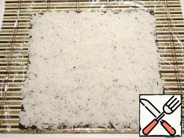 Take a sheet of nori, spread it on a bamboo Mat, covered with film. On top of the nori with wet hands evenly spread the rice thickness of about 0.5-0.4 cm