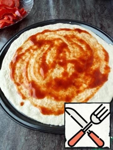 Separate one part from the test.
Sheet pizza a little grease with vegetable oil. With your hands flatten the dough into a thin layer.
Apply tomato sauce to the dough, but leave the edge clean.