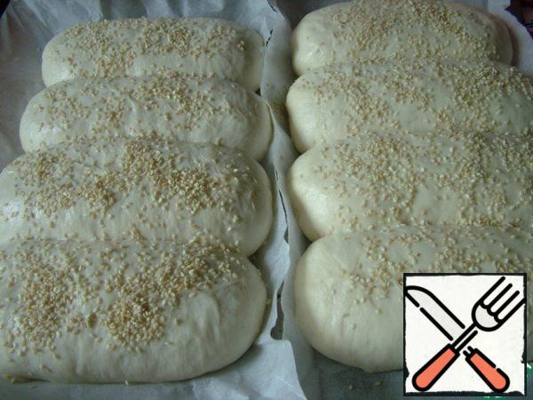 We shift the buns on a baking sheet, sprinkle with milk from the spray and sprinkle with sesame seeds.
