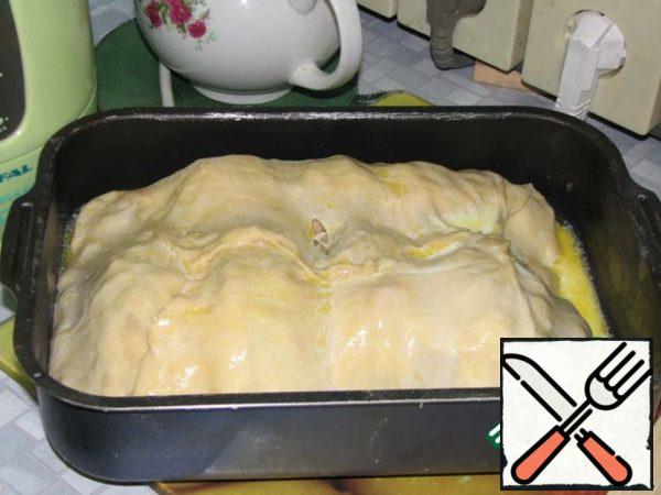 The two remaining pieces of dough should be molded together and rolled out of them into a square with a side of 50 cm . Grease the baking dish with oil and put a large sheet of dough on it. Place the resulting rolls tightly to each other in a mold on a layer of dough. Cover the rolls with the edges of a large sheet of dough and lightly pinch the edges. Mix the remaining melted butter with milk and pour the resulting mixture over the cake.
