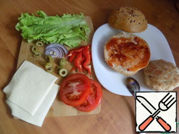Using the example of one chicken burger, I'll show you how I assemble it. We will need 1 bun, 1 cutlet, 2 slices of sandwich cheese. I take cheese without any additives, creamy and of course better. Cut a tomato across, we will need 2 slices, sweet pepper strips - 4 or 5 pieces. Three olives, cut into rings, a few pieces of finely chopped red onion and 2 lettuce leaves. Chili sauce. If you are going to cook for children, the sauce can not be added to the ingredients.
