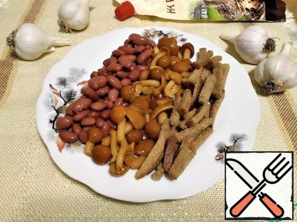 Crackers is better to take sharp! With mustard, horseradish, or garlic. And rye, they do not soak longer.Beans and mushrooms washed and spread in a plate. There we add rusks. Before serving, squeeze out the cloves of garlic. And add mayonnaise. All thoroughly mix!  