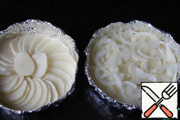 While the meat is in the refrigerator, make round molds from foil folded in several layers, lubricate the molds with vegetable oil. Place them on a baking tray.
Cut the potatoes into thin slices and put them in molds. Cut the onion into rings that are too thin.