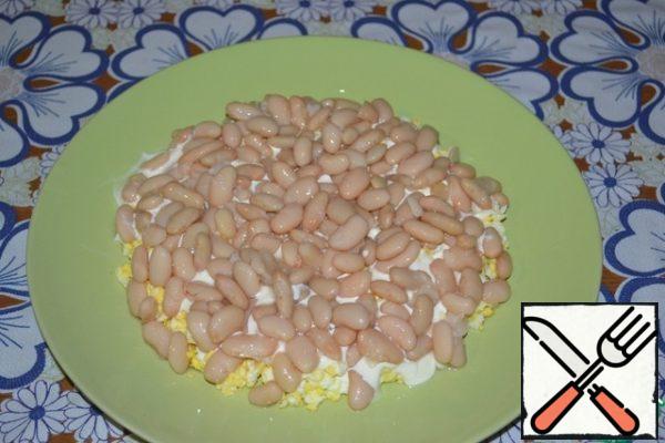 Drain the liquid from the canned white beans. Put on a dish with the next layer.