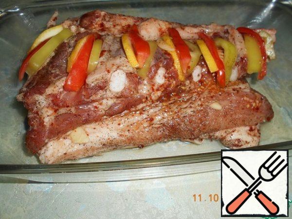 Cut the garlic into plates, pierce the meat from the sides with a sharp knife and insert the garlic into the punctures. Make incisions along the ribs from above and insert slices of tomato, lemon and sweet pepper into them. Put the meat in a baking dish, greased with oil.
