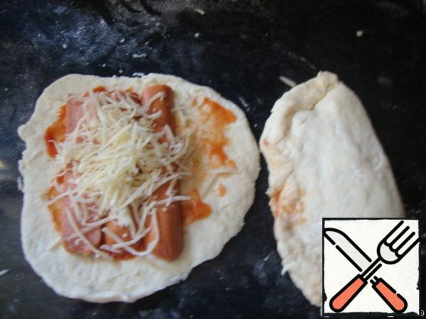 Divide the dough into 8 parts, roll out each thinly, lay out your filling: I smeared with ketchup, put the sausages, sprinkle with cheese; then close like pies.
