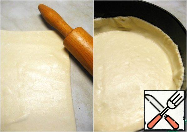 Defrost the dough, roll out slightly and put in a greased detachable form d=26 cm. Make the bumpers. Excess dough is cut off.