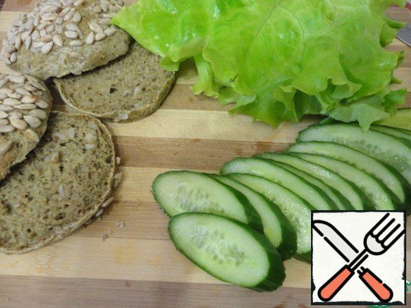 Wash the cucumber and lettuce leaves, dry them. Cut the cucumber into slices. Cut the buns in half.
