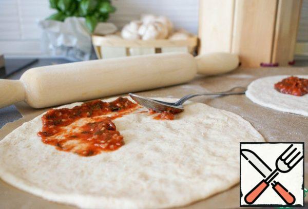 Grease the base with sauce, sprinkle with dry oregano. At this stage, you can leave the dough for another 15-30 minutes for proofing.