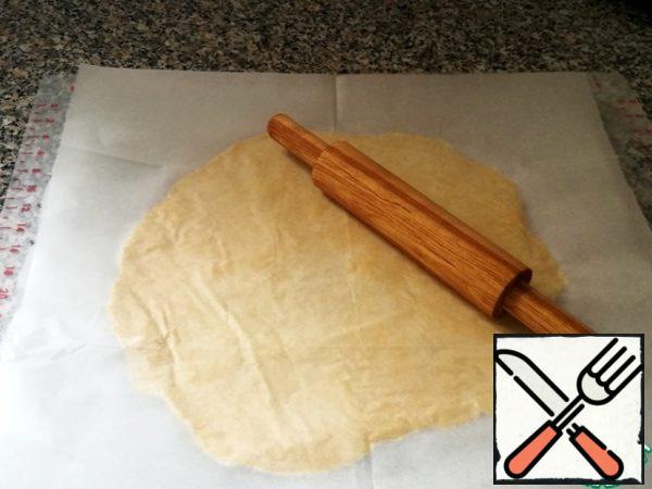 Get the dough out of the fridge and roll it in a circle, the size is slightly larger than the diameter of your cake mold, you need to take into account the height of the bumpers.
It is more convenient to roll out the dough between two layers of baking paper. First, spread the dough on the paper with your hands and then roll it out with a rolling pin.
Once the dough is rolled to the desired size, we need to carefully remove the top layer of paper. Chop the dough with a fork. The dough together with the lower layer of baking paper to transfer into a baking dish.
Now is the time to align the dough and form the bumpers, tightly pressing the dough to the walls of the mold. At this stage, you do not need to strive for beauty, let the sides be of different heights.