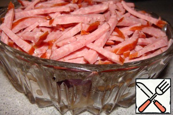 Cut the sausage into thin strips - this is the third layer. Cover the salad with a film or lid, leave to soak for a few minutes.