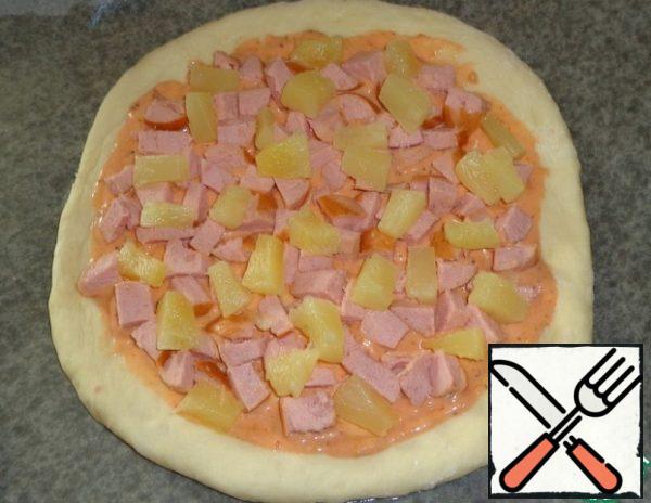 Roll out the dough into a round cake. Put on a baking sheet with parchment paper. Grease the sauce. Pineapples and sausage cut into cubes. Scatter the filling on the sauce.