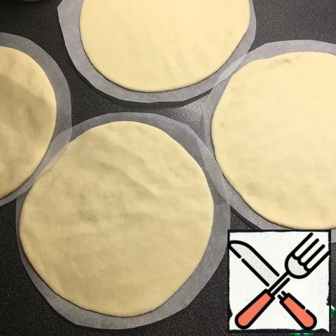 Each ball of dough with a rolling pin is rolled into a cake is not very thin, the thickness of about 3-4 mm, diameter 15-16 cm. Shift each piece on a sheet of parchment.
