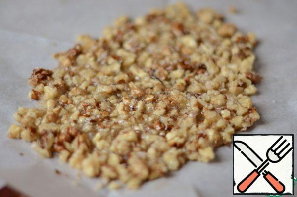 Dissolve 100 g of sugar with water in a saucepan with a thick bottom over low heat, as soon as the sugar begins to caramelize, add the nuts, then pour the resulting mass on the parchment and cool.