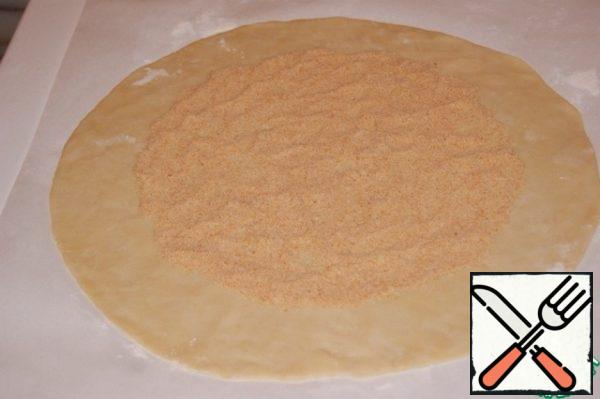 On baking paper, lightly sprinkled with flour, roll out the dough into a circle with a diameter of 34 cm. Step back from the edge by 4 cm and spread the crackers over the remaining surface.
