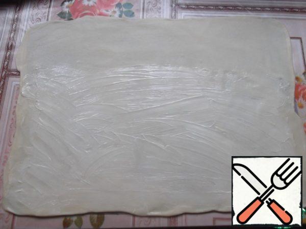 Roll out a very thin dough. I have a silicone mat, but you can use a towel, sprinkle it well with flour (if the dough is rolled out just on the table, then it will be very difficult to fold the strudel and put it on a baking sheet). With softened butter (about 20-30 g), lubricate the dough layer, except for about 10 cm from one edge (this will be a seam).
