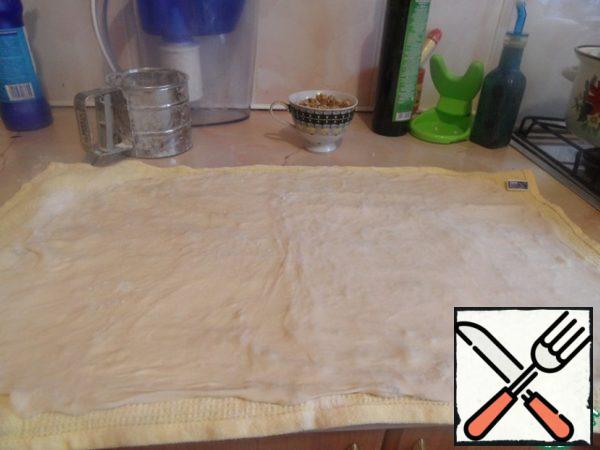Clean kitchen towel abundantly sprinkle with flour, put the dough on it and not too thinly roll it into a rectangle. Then, with your hands, pull the dough in a circle until it becomes transparent like tissue paper.