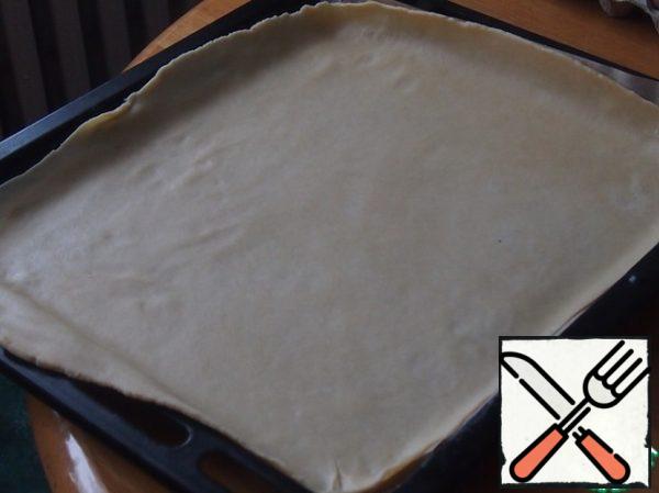 Divide the dough into two parts and roll out two rectangles the size of a baking sheet, an ordinary large baking sheet, for the entire oven. Cover the baking sheet with baking paper, lay out one part of the dough. The dough turns out to be very pleasant, it rolls out easily.
