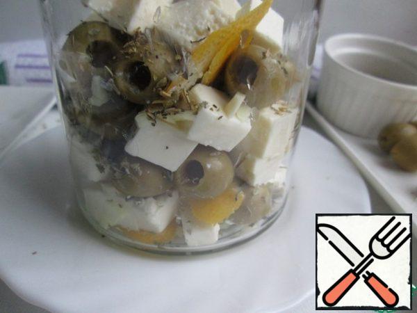 Put the cheese in a jar, alternating with garlic, strips of zest, paprika, olives and Provencal herbs.
