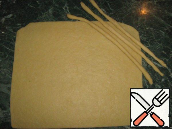 The approached dough is rolled out. Cut off the extra pieces of dough on the edge of the cake, giving the shape of a rectangle. From scraps of dough make the same strips to decorate the strudel.