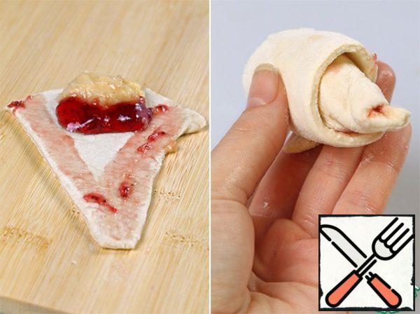 Now, on a wide part of the triangle, we put the cream, squeeze out a number of jam, they also lubricate a little edge of the dough, and you can and the whole piece.
And gently roll the croissant, trying to keep the stuffing from getting out.
Then, in addition, turn the corners with your fingers.