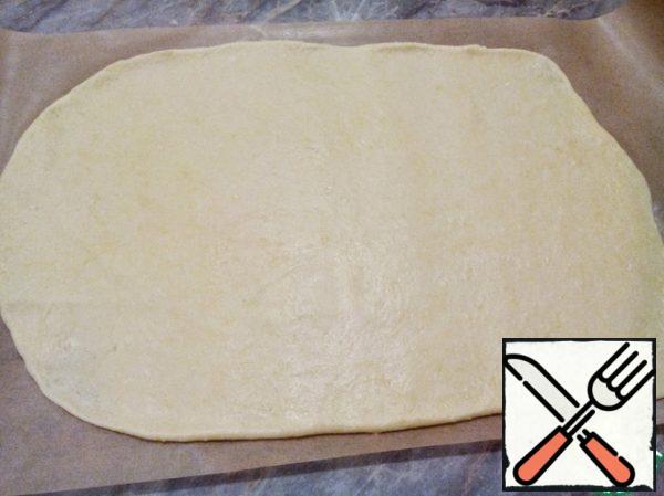 Take the baking paper of the desired size and smear with a small amount of vegetable oil or flour. Roll out the dough on parchment paper in a thin layer.
