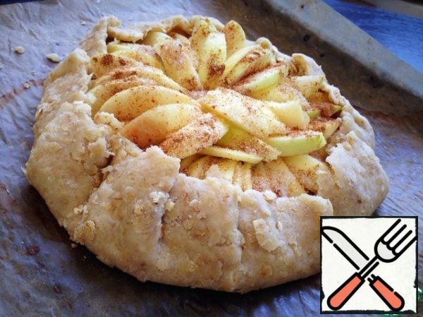 Retreating from the edge of 5 cm, sprinkle the center of the biscuits corn starch. Put the Apple slices in a circle overlap, just retreating from the edge of 5 cm.
Sprinkle apples with sugar, cinnamon and ginger. The edges of the dough wrap inside, forming a galette.
